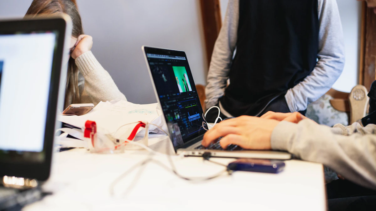 People gathered at a shared table with laptops, papers and a phone.